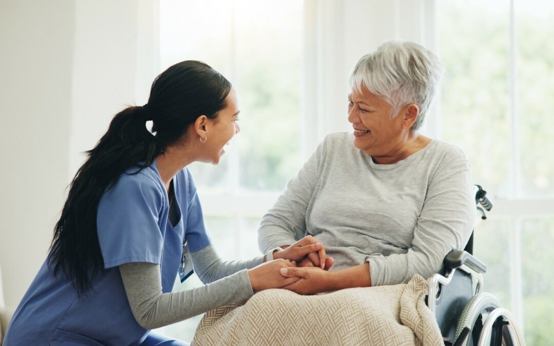 A palliative care worker holds the hands of a smiling patient.